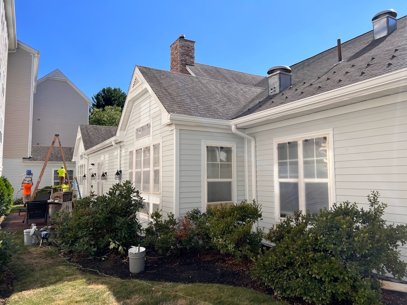 Exterior painting project by N&M Services in progress: the home's siding prepped and windows protected with plastic while the crew works around the building.